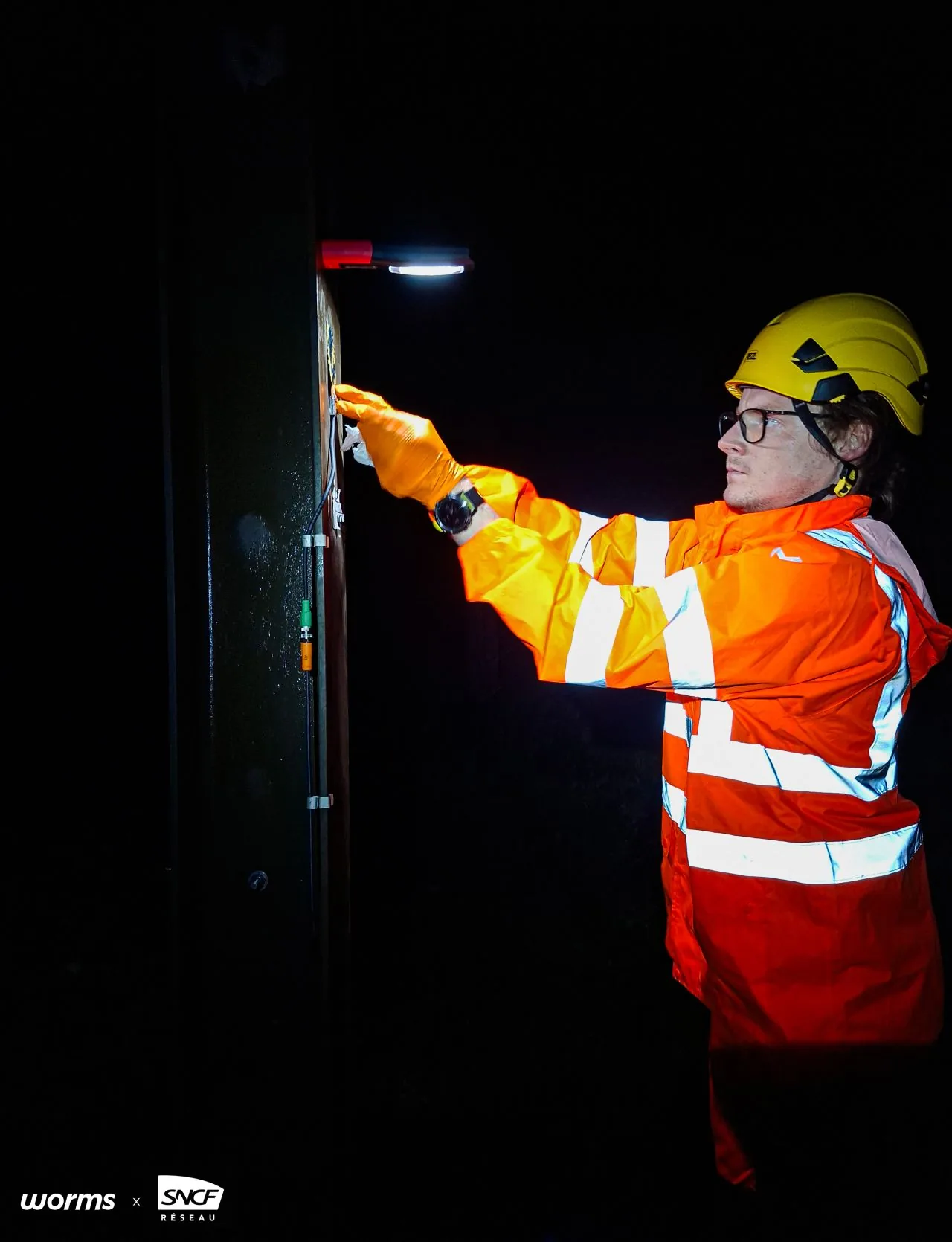 A technician in high-visibility gear installing a sensor at night