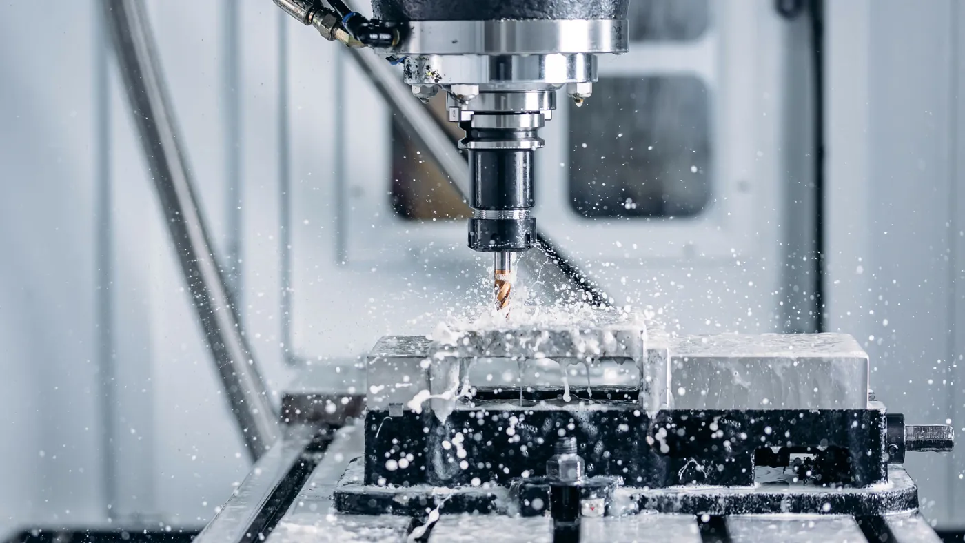 A CNC milling spindle cutting a metal part under coolant.